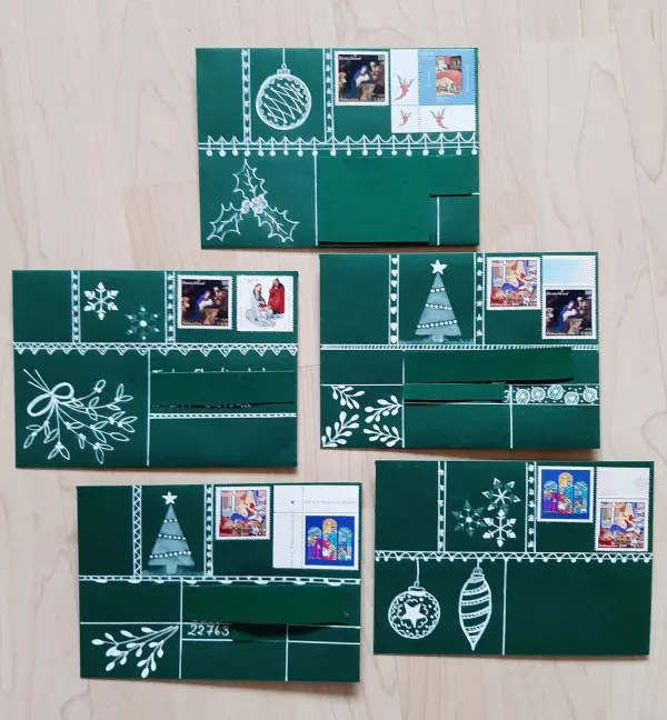Grüne Weihnachtskarten sind kunstvoll gefaltet mit Tannenbaum-Motiven und verzierten Briefmarken auf einem Holztisch.