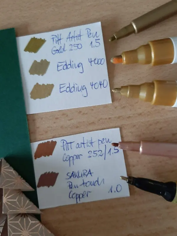 Gefalteter Tannenbaum liegt neben Farbkarten und Stiften, die verschiedene Farben für eine Weihnachtskarte zeigen.