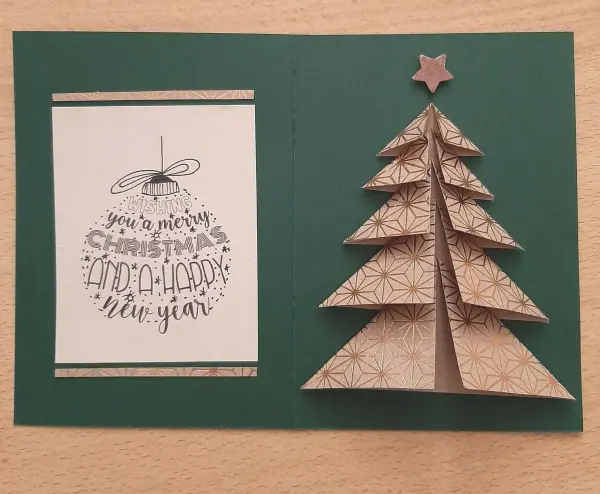 Eine gefaltete Weihnachtskarte zeigt einen dreidimensionalen Tannenbaum aus braunem Papier und einen Grußtext.