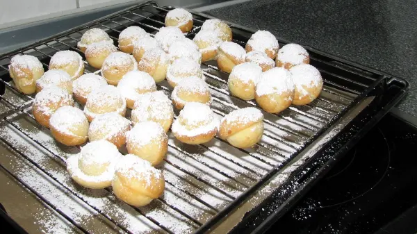 Kleine, runde Frischkäse-Schneebällchen liegen auf einem Gitterrost und sind mit Puderzucker bestäubt.