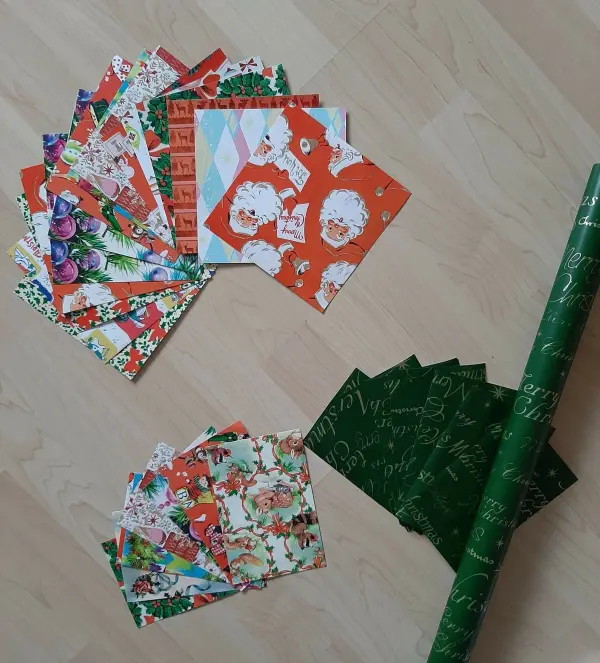 Bunte Papierrollen und Karten liegen auf einem Holztisch, bereit zur Herstellung eines Weihnachtskranzes mit Tannendekor.