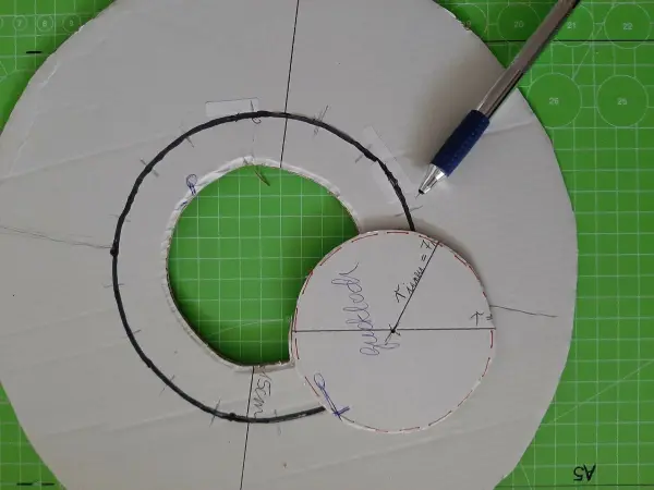 Ein Pappkreis wird mit einem Stift bearbeitet, um Formen für einen Weihnachtskranz aus Papierrollen zu zeichnen.