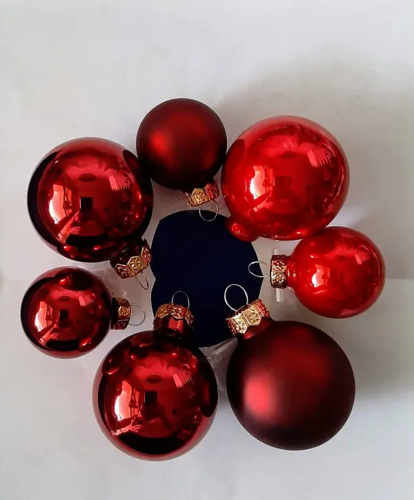 Ein roter Weihnachtskranz aus glänzenden Tannenbaumkugeln ist auf einem weißen Hintergrund angeordnet.