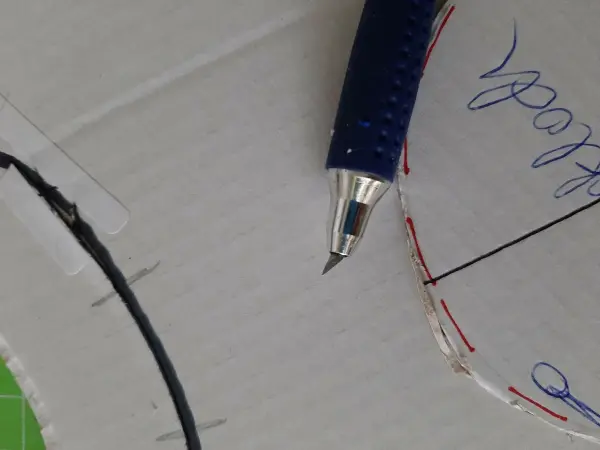 Ein blauer Stift liegt knapp über einem Karton mit gezeichneten Linien, während ein kreatives DIY-Projekt entsteht.