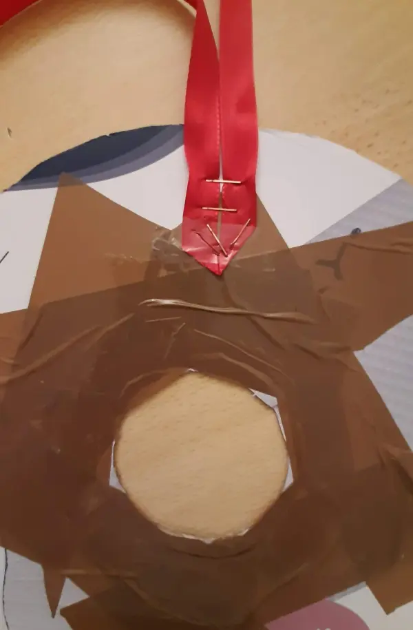 Ein Weihnachtskranz aus Papierrollen wird mit einem roten Band aufgehängt, während er auf einem Tisch liegt.