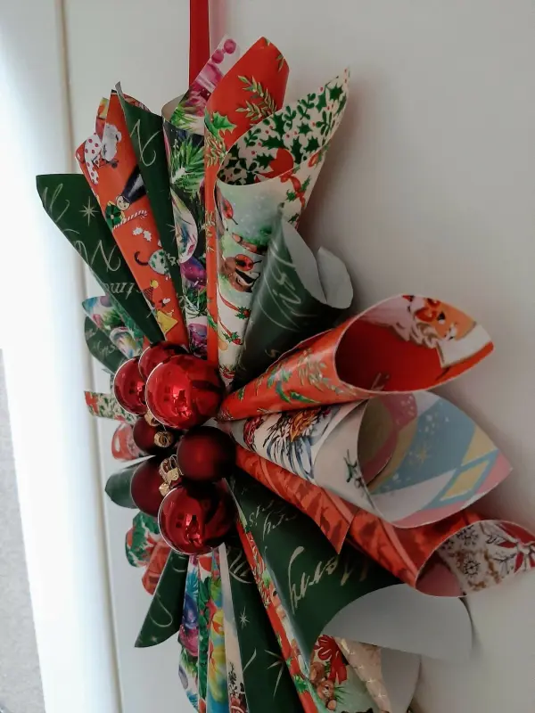 Ein bunter Weihnachtskranz aus Papierrollen und Tannenbaumkugeln hängt an einer Wand und verleiht dem Raum festliche Stimmung.