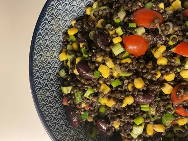 Ein bunter Salat mit Belugalinsen und Mais wird in einer stylischen Schüssel angerichtet und zeigt eine frische Mischung aus Gemüse.