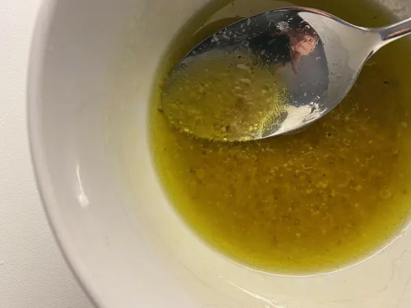 Ein Löffel rührt in einer Schüssel mit goldener Vinaigrette, die für den Belugalinsen-Salat mit Mais vorbereitet wird.