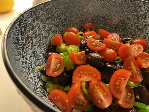 Ein bunter Belugalinsen-Salat mit frischen Kirschtomaten und grünen Zwiebeln in einer dekorativen Schüssel.