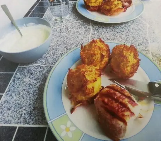 Auf einem Teller liegen goldbraune Rösti-Muffins neben einem Stück Fleisch, mit einem Beilagensalat in einer Schüssel.