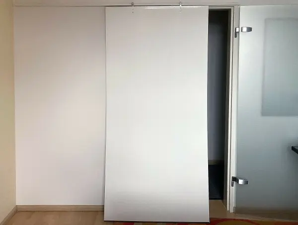 Eine Verdunkelungstür auf Rollen hängt in einem modernen Raum und schließt den Zugang zu einer angrenzenden Tür.