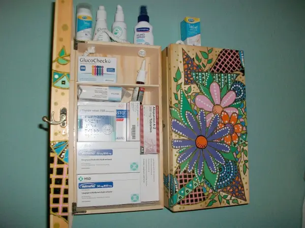 Eine dekorative Holzkiste, die mit bunten Blumenmotiven bemalt ist, dient zur Aufbewahrung von Medikamenten und Pflegeprodukten.