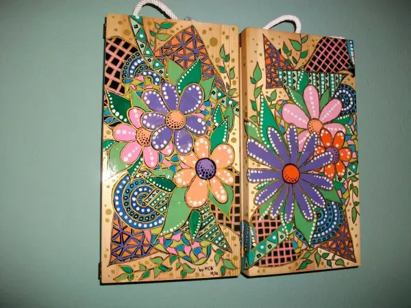 Holz Weingeschenkkisten sind bunt bemalt mit Blumenmustern und hängen dekorativ an einer Wand in einem hellen Raum.