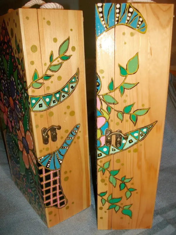 Schöne Holz-Weingeschenkkisten zeigen florale Muster und Verzierungen, die kreativ bemalt sind, auf einem blauen Stoff.