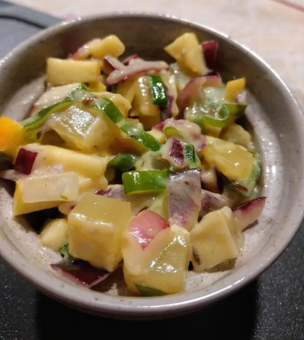 Ein bunter Salat aus Handkäse, gewürfeltem Gemüse und einer cremigen Sauce befindet sich in einer kleinen Schüssel.