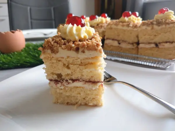 Eine exquisite Frankfurter Kranz Schnitte steht auf einem Teller, dekoriert mit Sahne und Kirschen, im hellen Hintergrund.