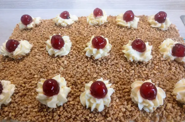 Eine dekorative Frankfurter Kranz Schnitte mit Sahnehauben und Kirschen auf einer knusprigen Nussbasis.