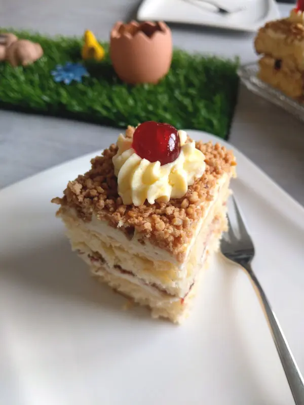 Eine üppige Frankfurter Kranz Schnitte liegt auf einem weißen Teller, dekoriert mit Sahne und einer Kirsche, umgeben von österlicher Deko.