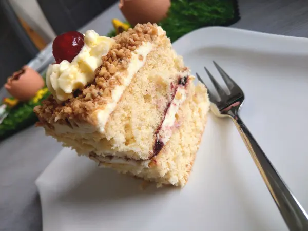 Süßer Frankfurter Kranz Schnitte liegt auf einem Teller, garniert mit Kirsche und Sahne, umgeben von fröhlichem Dekor.