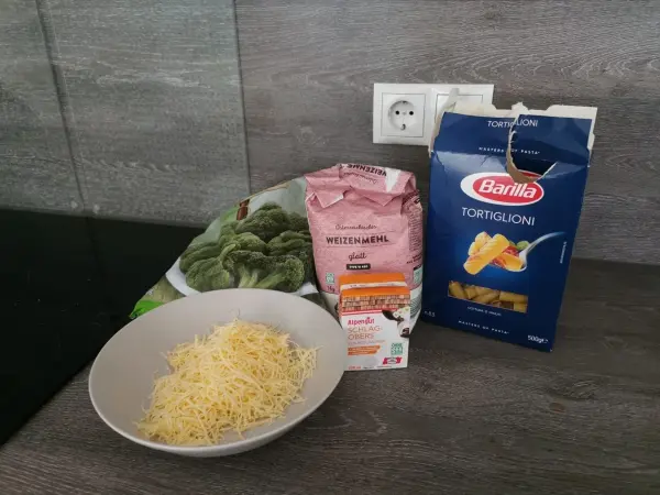 Tortiglioni und Brokkoli liegen zusammen mit Weizenmehl und Sahne in einer modernen Küche auf dem Tisch bereit.