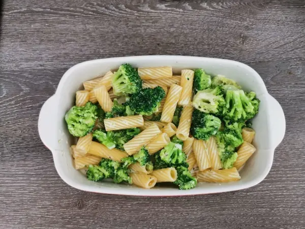 Tortiglioni und Brokkoli sind in einer weißen Schüssel angerichtet, umgeben von einem holzähnlichen Tisch.