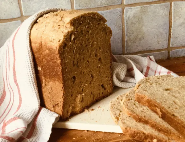 Ein frischer Laib Brot steht auf einem Brett und hat einige geschnittene Scheiben daneben, umgeben von Küchenutensilien.