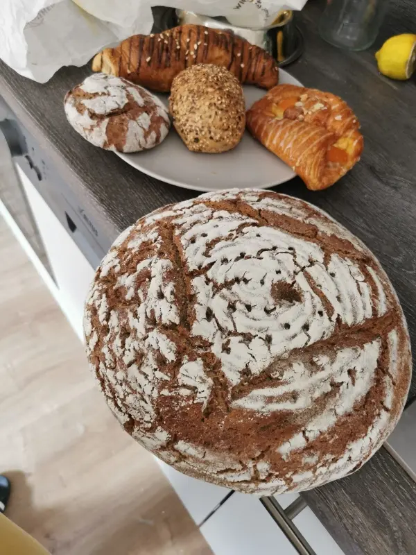 Ein Laib Brot liegt auf einer Küchentheke, umgeben von verschiedenen Backwaren auf einem Teller, die appetitlich aussehen.