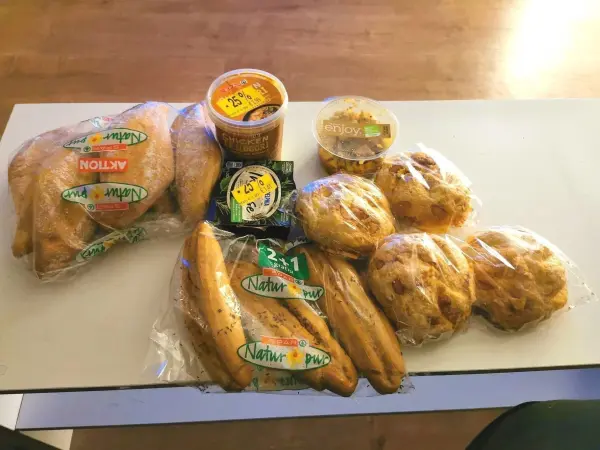 Auf einem Tisch liegen verpackte Lebensmittel: Brötchen, Bananen und Dips. Eine Aktion des Lebensmittelrettens verdeutlicht den Kontext der Verwertung.