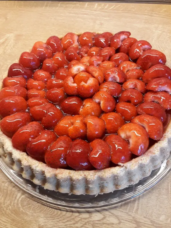Ein Erdbeerkuchen mit glänzenden, frischen Erdbeeren auf einem Dinkeltortenboden steht auf einem Holzuntergrund.