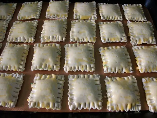 Gebackene Blätterteigtaschen liegen auf einem Backblech und sind gleichmäßig mit Eistreif bestrichen.