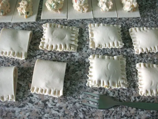 Gefüllte Blätterteigtaschen liegen auf einer Arbeitsfläche, umgeben von anderen Teigstücken und einem Gabel.