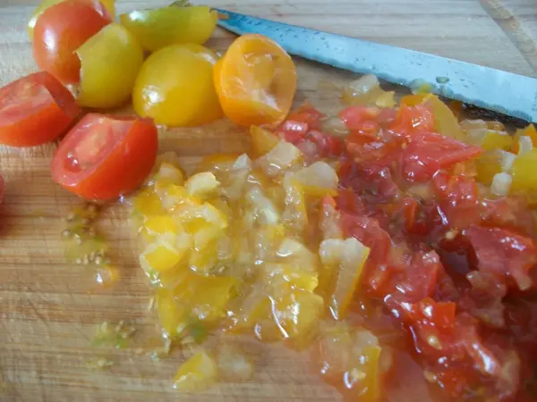 Diced, juicy Tomaten und gelbe Paprika liegen auf einem Schneidebrett, während ein Messer daneben platziert ist.