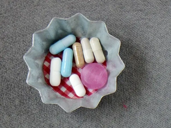 In einer Schale liegen verschiedene große Tabletten und Kapseln, umgeben von einem rot-weißen Tuch.