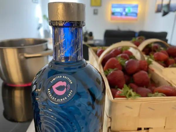 Eine Flasche blauer Limes steht neben einem Topf und frischen Erdbeeren in Körben, ideal für die Grillparty.