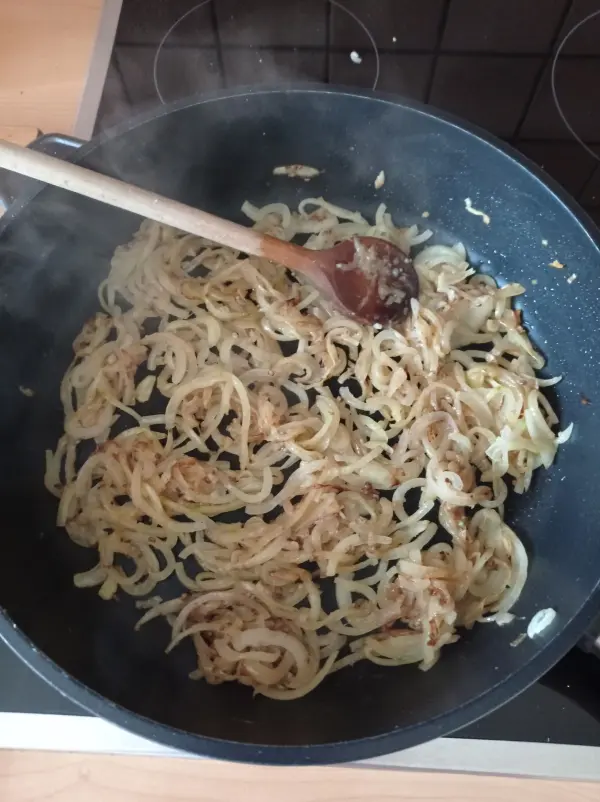 In einem Topf werden goldbraune Zwiebeln unter Dampf mit einem Holzlöffel gerührt, bereit für die französische Zwiebelsuppe.