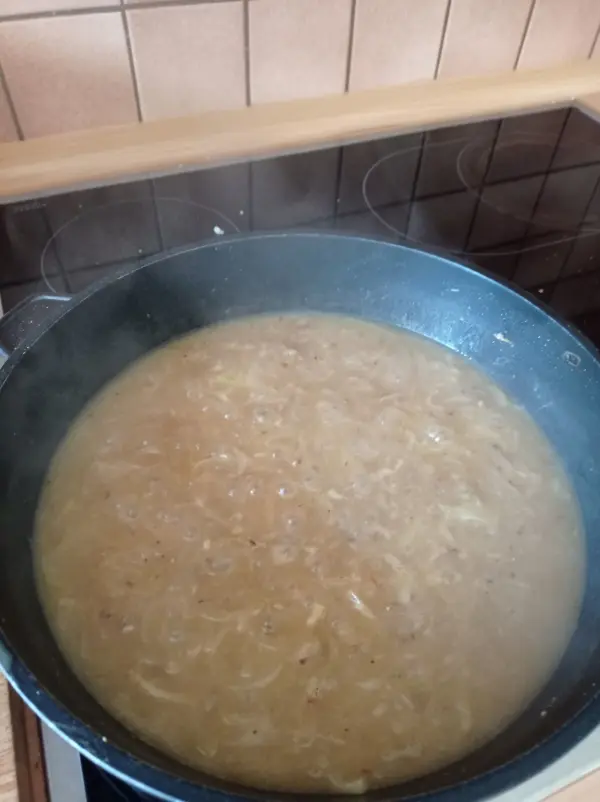 Ein Topf mit dampfender französischer Zwiebelsuppe kocht auf einem Herd in einer modernen Küche.