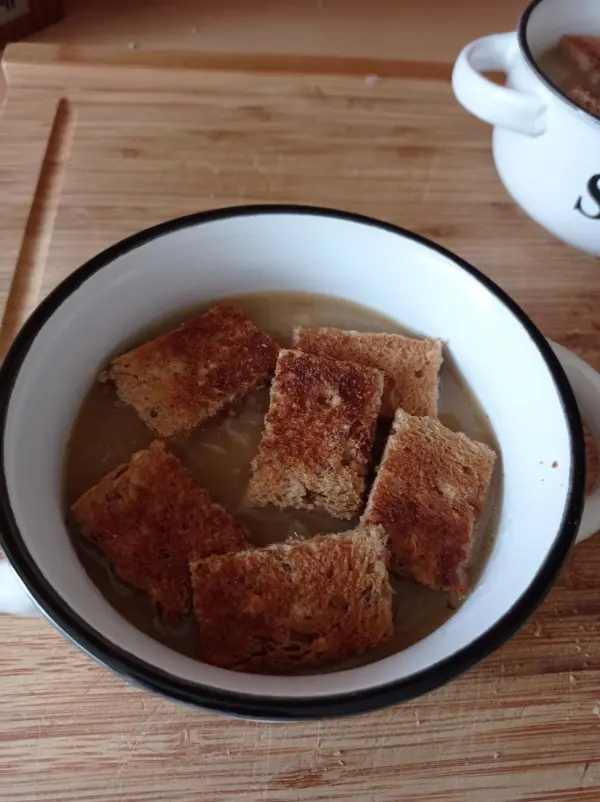 Eine Schüssel mit französischer Zwiebelsuppe, belegt mit gerösteten Brotscheiben, steht auf einem Holzbrett.