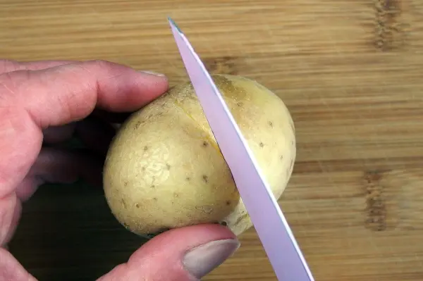 Eine Hand hält eine Kartoffel, während ein Messer an der Schale einritzt, um das Schälen zu erleichtern.
