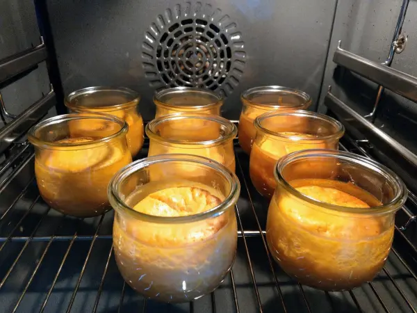 Im Ofen backen mehrere Gläser mit Käsekuchen, die goldbraun und leicht geschwollen aussehen.