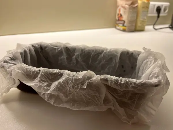 Ein runder, gefetteter Gärkorb mit Backpapier steht auf einer weißen Oberfläche in einer modernen Küche.