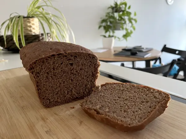 Ein geschnittenes, knuspriges Roggenvollkorn-Sauerteigbrot liegt auf einem Holzbrett in einer modernen Küche.