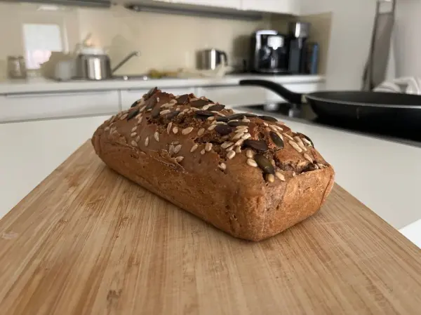 Ein knuspriges Roggenvollkorn-Sauerteigbrot liegt auf einem Holzbrett in einer modernen Küche mit hellen Möbeln.