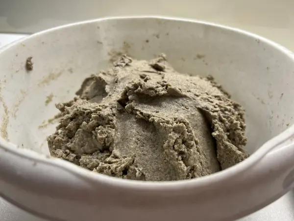 Ein dichter, brauner Roggenteig liegt in einer weißen Schüssel, bereit für die Verarbeitung zum Sauerteigbrot.