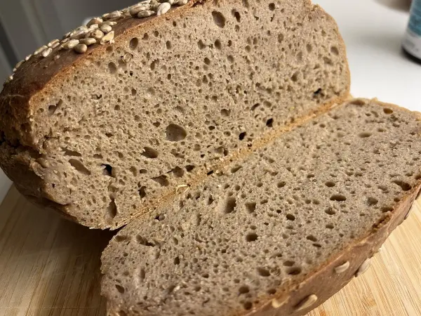 Ein frisch aufgeschnittenes Roggenvollkorn-Sauerteigbrot liegt auf einem Holzbrett, die Kruste ist knusprig und golden.