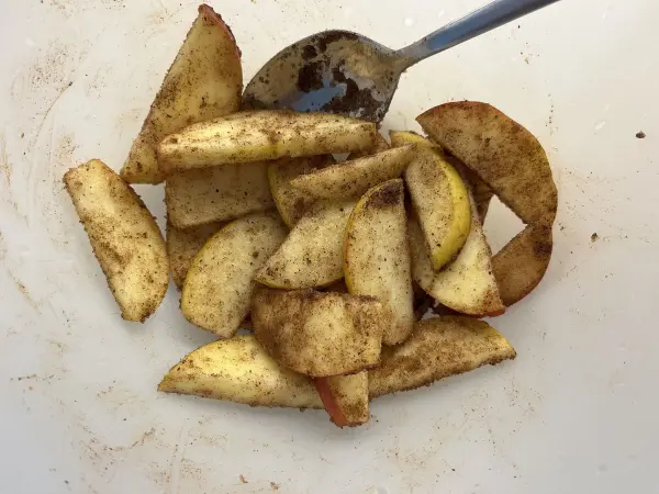 Geschnittene Äpfel liegen in einer Schüssel, bestreut mit Zimt, bereit zur Verwendung in einem Apfel-Joghurt-Kuchen.