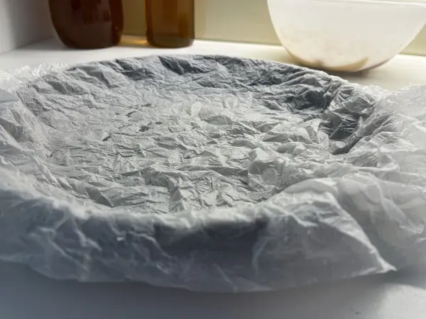 Ein zerknitterter, feuchter Backpapierkreis liegt auf einer Fläche, um Apfel-Joghurt-Kuchen zuzubereiten.