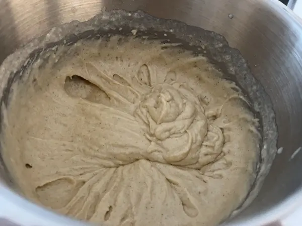 Sahneartige Masse wird in einer silbernen Schüssel vorbereitet, ideal für einen saftigen Apfel-Joghurt-Kuchen mit Zimt.