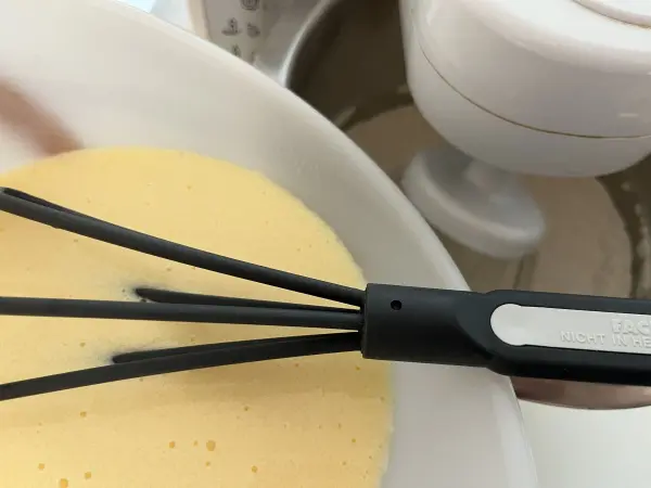 In einer Schüssel befindet sich cremiger Teig zum Apfel-Joghurt-Kuchen, während ein Rührbesen ihn gründlich vermischt.