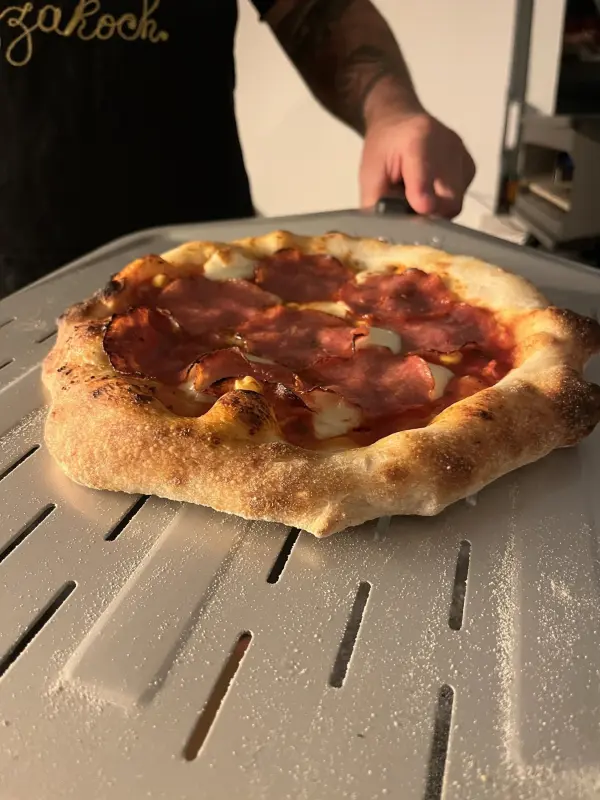 Eine frisch gebackene Pizza mit knusprigem Rand liegt auf einem Blech, während sie zum Servieren gehalten wird.