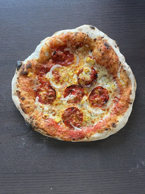 Eine frisch gebackene Pizza liegt auf einem dunklen Holztisch und duftet köstlich nach Tomatensauce und Käse.